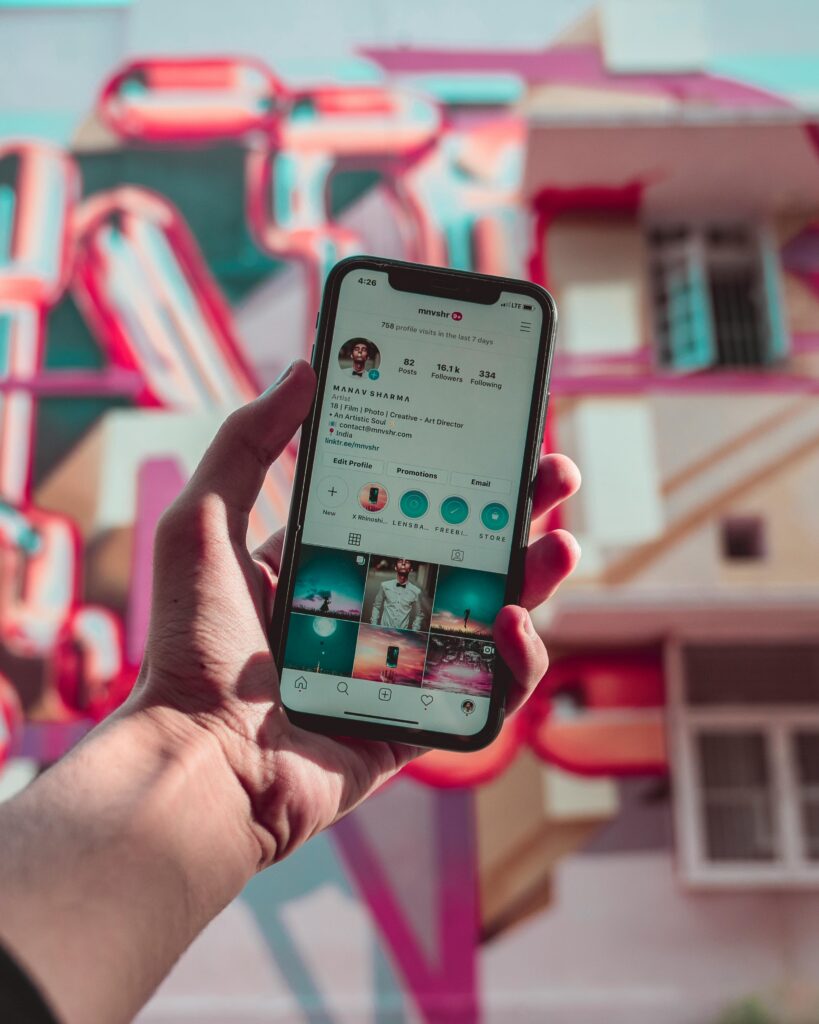 pexels-photo-2971692-2971692 A hand holds a smartphone displaying social media, set against a colorful urban mural.